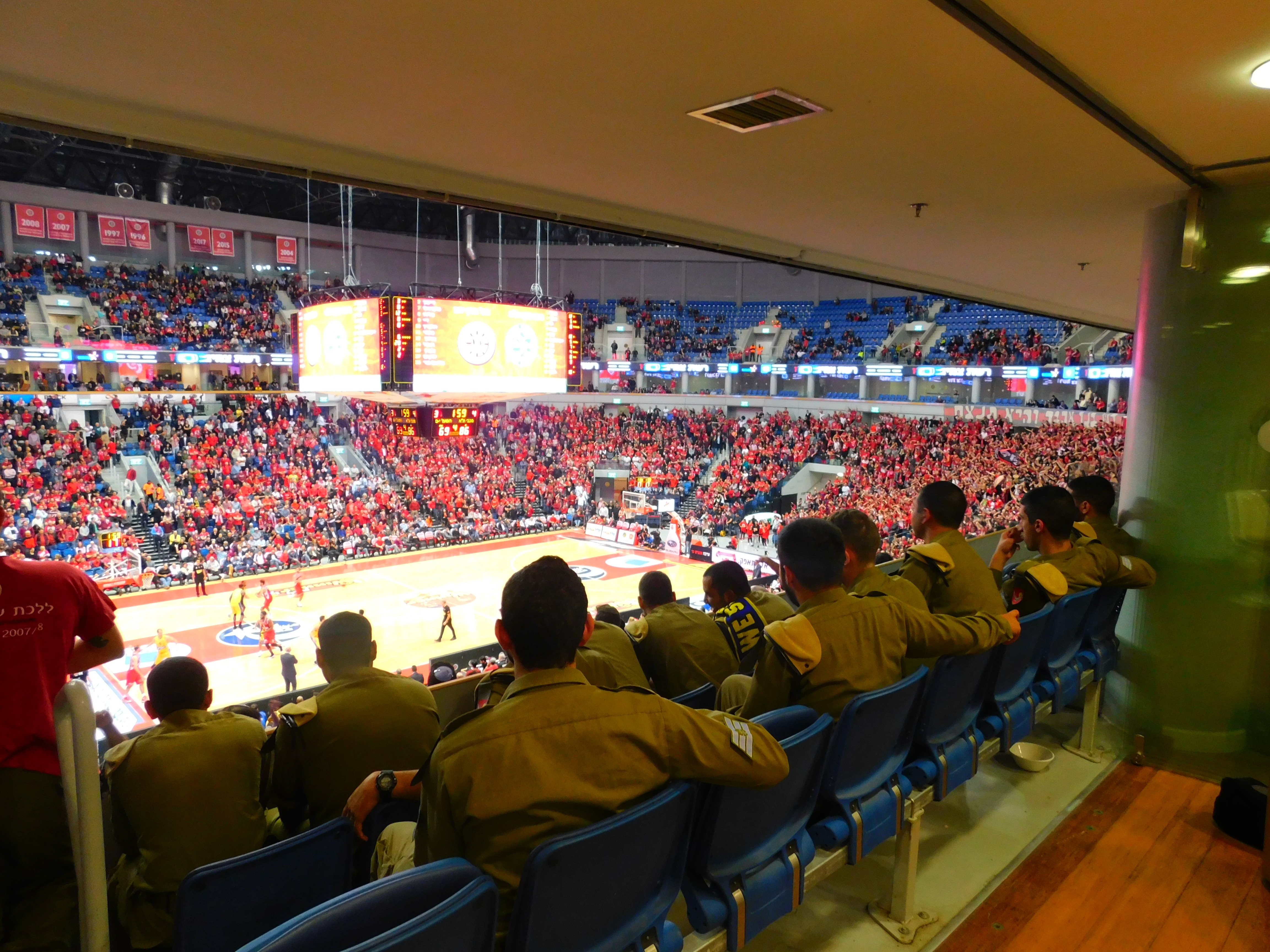 A group of IDF soldiers enjoy watching a basketball game.